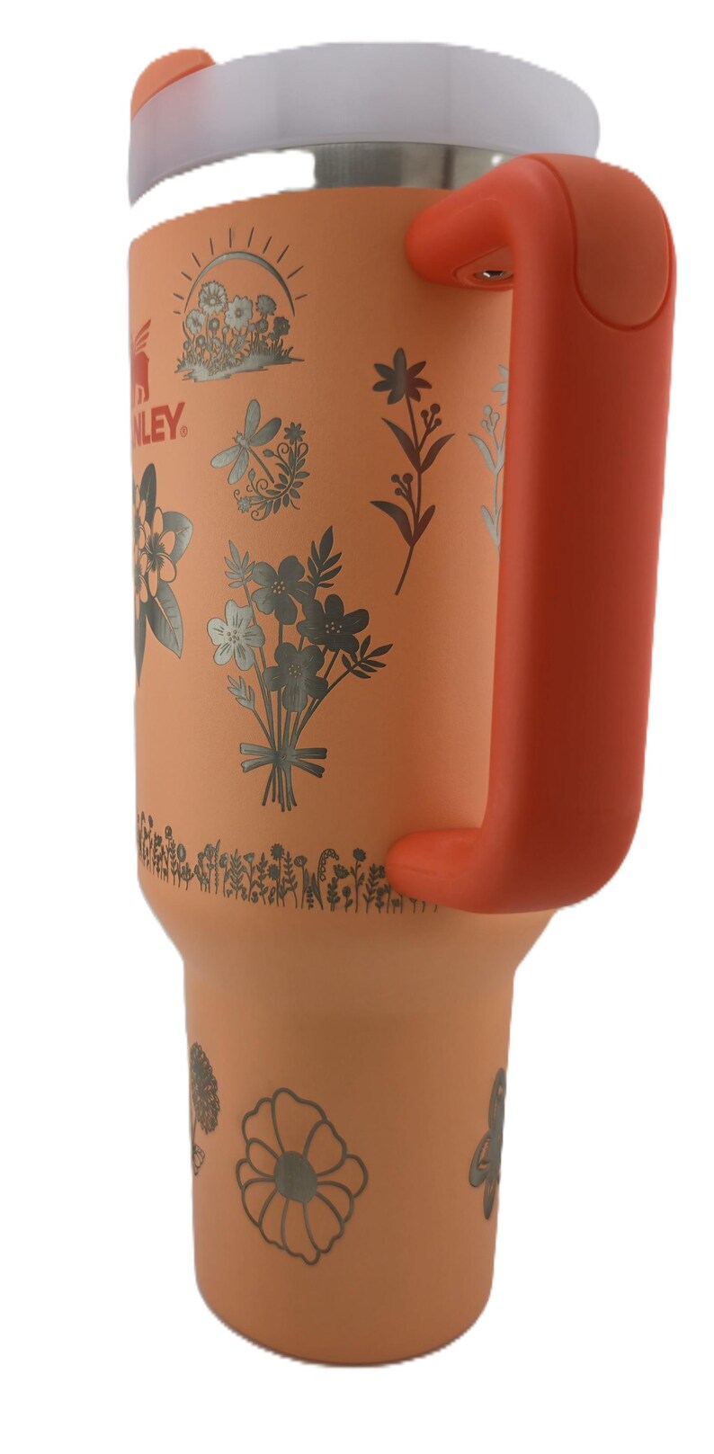 May include: A peach-colored insulated tumbler with a white lid and orange handle. The tumbler is decorated with silver floral designs and the brand name "Stanley". The handle is a vibrant orange color.