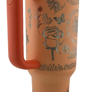 May include: An orange insulated tumbler with a white lid and orange handle. The tumbler is decorated with floral and butterfly designs, along with the words "Be Kind, Be True".