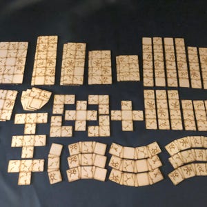 May include: A selection of laser-cut wooden dungeon tiles in various shapes and sizes. The tiles are light brown with an engraved stone pattern. The set includes square, rectangular, and curved pieces for building diverse game environments.