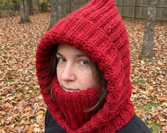 May include: A vibrant red knitted hood and cowl set. The hood features a ribbed design and a pointed top, while the cowl wraps around the neck. The set is made of a thick, warm yarn, perfect for cold weather.