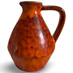May include: A ceramic pitcher with a handle, featuring a glossy, mottled glaze in shades of orange and brown. The pitcher has a rounded body and a spout for pouring. This decorative piece is suitable for serving beverages.