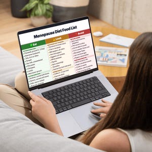 May include: A laptop displays a "Menopause Diet Food List" with sections for foods to eat, limit, and avoid. The screen shows a list of foods, including flaxseeds, tomatoes, and spicy foods. The laptop is on a person's lap.