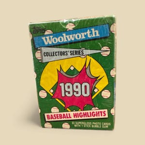 May include: Sealed 1990 Woolworth Collectors' Series baseball card pack. The pack features a green background with baseballs, a blue banner with "Woolworth" in white, and a red burst with "1990". The text "Baseball Highlights" is also visible.