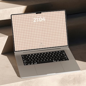 May include: A silver laptop with a black keyboard and a screen displaying a light pink and white gingham pattern. The screen shows the time 21:04 in white text centred at the top. The device has a thin bezel and a large trackpad below the keys.