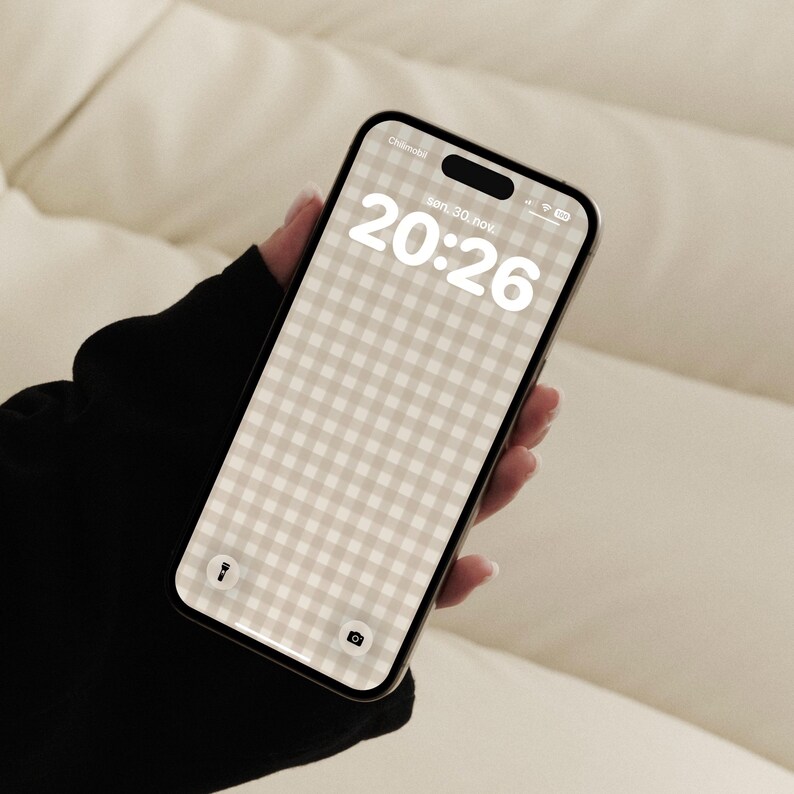Pode incluir: Um smartphone exibindo uma tela de bloqueio com um papel de parede de padr&atilde;o xadrez vichy bege e branco. A tela mostra a hora 20:26, a data Son. 30. nov., um &iacute;cone de lanterna e um &iacute;cone de c&acirc;mera. O dispositivo tem uma moldura preta.