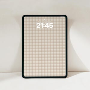 Pode incluir: Um tablet com moldura preta exibindo um padr&atilde;o de xadrez vichy bege e branco na tela. A tela mostra a hora 21:45 e o texto Sveip opp for &aring; l&aring;se opp no centro superior. O dispositivo possui cantos arredondados e uma borda fina ao redor.