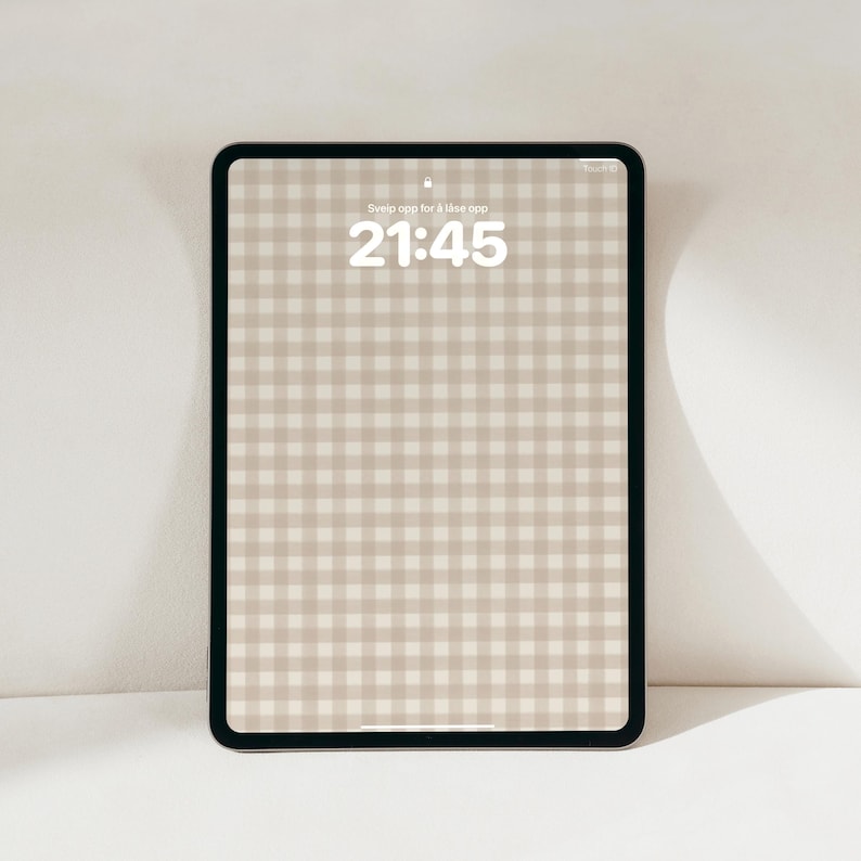 Pode incluir: Um tablet com moldura preta exibindo um padr&atilde;o de xadrez vichy bege e branco na tela. A tela mostra a hora 21:45 e o texto Sveip opp for &aring; l&aring;se opp no centro superior. O dispositivo possui cantos arredondados e uma borda fina ao redor.