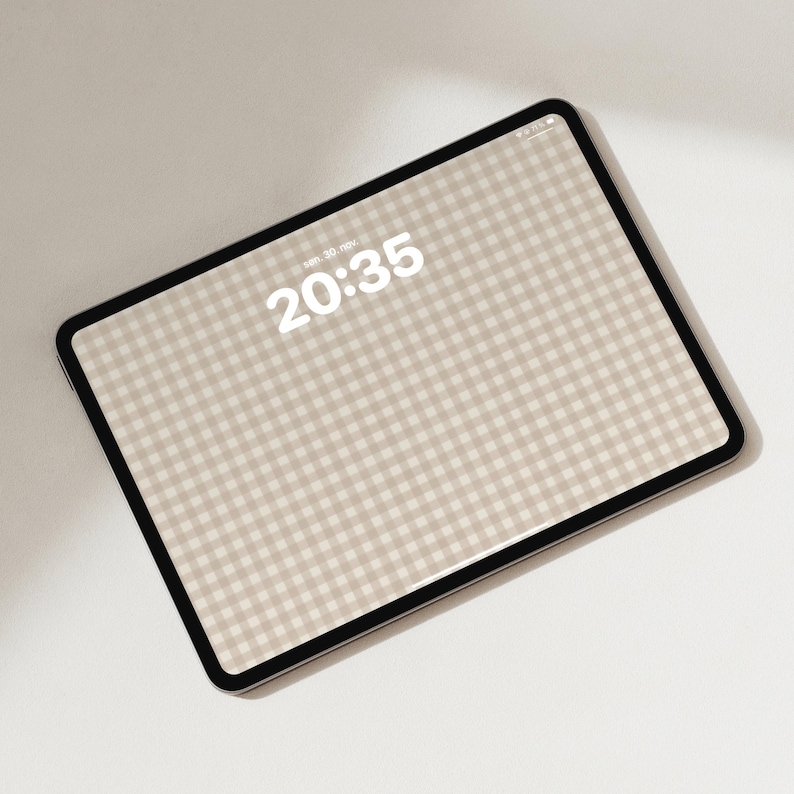 Pode incluir: Um tablet com moldura preta exibindo um padr&atilde;o xadrez vichy bege e branco na tela. O rel&oacute;gio digital no visor mostra a hora 20:35 e a data sen. 30. nov. O dispositivo est&aacute; posicionado em &acirc;ngulo sobre um fundo liso e claro.