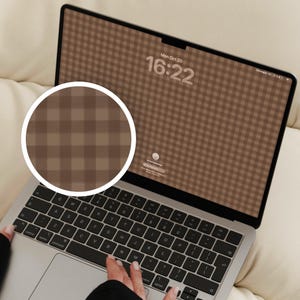 May include: A silver laptop with a black keyboard and a screen displaying a brown and tan gingham check pattern wallpaper. The screen shows the date Mon Oct 20 and the time 16:22. A circular inset shows a magnified view of the brown plaid pattern.