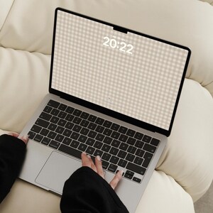 Pode incluir: Um port&aacute;til prateado com teclado preto e um ecr&atilde; que exibe um fundo com padr&atilde;o de xadrez vichy bege e branco. O ecr&atilde; mostra a hora 20:22 e a data em texto branco. O dispositivo apresenta uma moldura fina e um layout de teclado QWERTY.