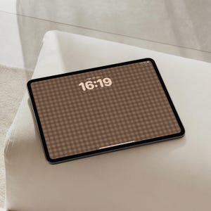 May include: A tablet device with a dark frame and a screen displaying a brown and white gingham pattern background. The screen shows the time 16:19 in a bold, light-coloured font centred at the top, with a thin white horizontal bar at the bottom.