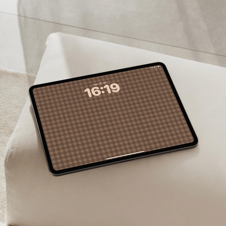May include: A tablet device with a dark frame and a screen displaying a brown and white gingham pattern background. The screen shows the time 16:19 in a bold, light-coloured font centred at the top, with a thin white horizontal bar at the bottom.