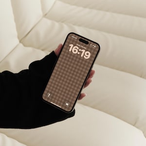 May include: A black smartphone displaying a brown and white gingham patterned wallpaper on the screen. The lock screen shows the time 16:19, the date man. 20. okt., a signal strength indicator, and battery icon. The device has a black frame.