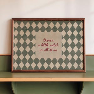 May include: A rectangular wall shelf with a green surface and light orange trim holds a framed print. The print features a dark green and beige diamond pattern with the text "there's a little witch in all of us" in red cursive lettering.