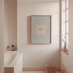 May include: A framed artwork with a light blue and white striped background and the word "Love" in red script. The artwork is displayed in a bathroom setting, with a neutral color palette and a woven basket.