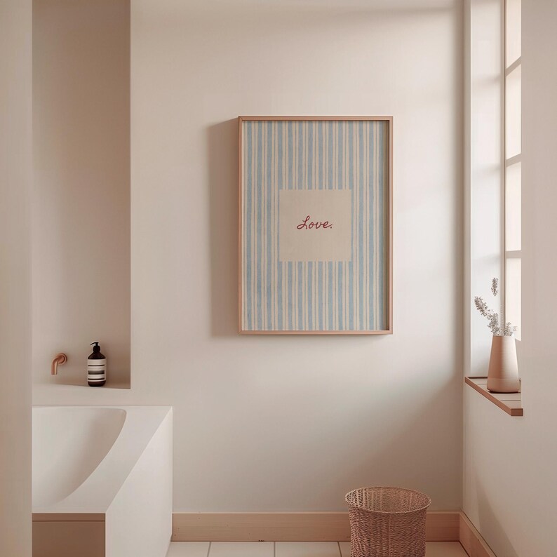 May include: A framed artwork with a light blue and white striped background and the word "Love" in red script. The artwork is displayed in a bathroom setting, with a neutral color palette and a woven basket.