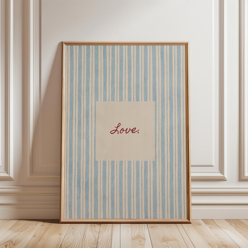 May include: Framed artwork with a light blue and white striped background. A square in the center features the word "Love" in a cursive, reddish-brown font. The frame is a light brown color.