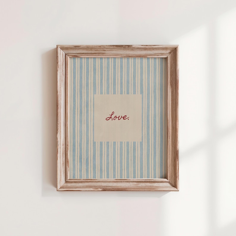 May include: A framed print with a light blue and white striped background. The center features a square with the word "Love" in red script. The frame is a distressed, light brown color, adding a vintage feel to the artwork.