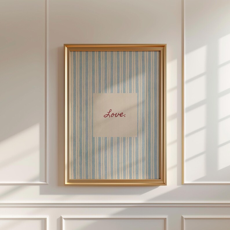 May include: A framed print with a gold-colored frame. The artwork features a light blue and white striped background with a square overlay. The word "Love" is written in red script within the square.