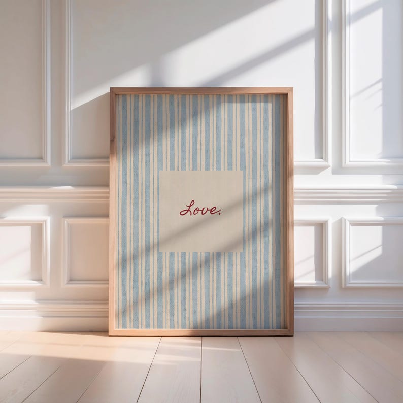 May include: A framed print featuring a light blue and white striped background with a beige square in the center. The word "Love" is written in red cursive script within the square. The frame is made of light brown wood.