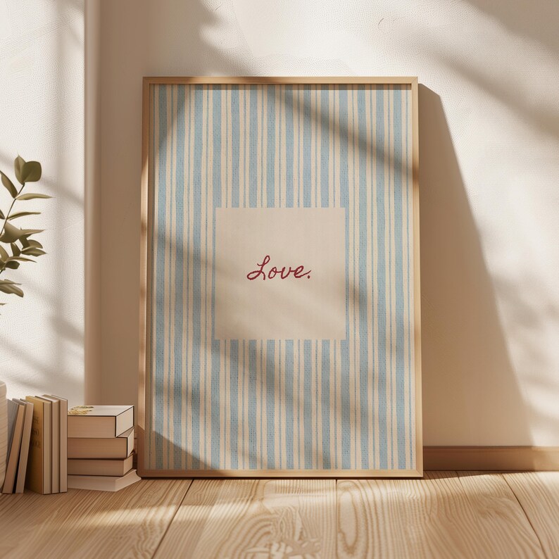 May include: A framed print with a light wood frame. The print features a blue and white striped background with a beige square in the center. The word "Love" is written in red script within the square.