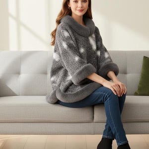 Pode incluir: Um poncho cinza com bolinhas brancas, gola e punhos de pele sintética. A modelo usa jeans azuis e botinhas pretas. O suéter tem um corte folgado e é adequado para climas mais frios.