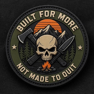 Peut inclure: Écusson circulaire avec le texte "BUILT FOR MORE" et "NOT MADE TO QUIT". Le design présente un crâne, une hache et un couteau croisés, des montagnes, un coucher de soleil et un feu de camp, dans des tons de noir, vert, orange et beige.