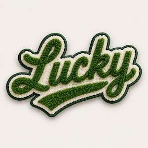 Könnte beinhalten: Ein grün-weiß gestickter Aufnäher mit dem Wort "LUCKY" in Schreibschrift. Der Aufnäher hat einen grünen Rand und einen weißen Hintergrund. Die Buchstaben sind ein strukturiertes, erhabenes Design.