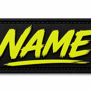 May include: A rectangular black patch with rounded corners and a stitched border. The word NAME is displayed in a bright yellow, brush-stroke style font with a horizontal line underneath, creating a high-contrast graphic design on the surface.