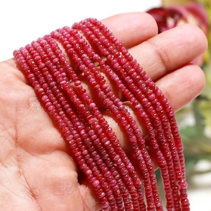 May include: A collection of multiple strands of small, round, deep red gemstone beads. The beads have a smooth, polished texture and a consistent, vibrant crimson hue, arranged in parallel lines to showcase their uniform size and shape.