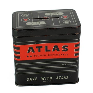 K&ouml;nnte beinhalten: Schwarze Metall-Sparb&uuml;chse mit einem rot-wei&szlig; gestreiften Design. Die Spardose hat einen Schlitz oben und tr&auml;gt die Aufschrift "ATLAS" in roten Buchstaben mit dem Text "RUGGED DEPENDABLE" darunter. Der Boden der Spardose tr&auml;gt die Aufschrift "SAVE WITH ATLAS" in wei&szlig;en Buchstaben.