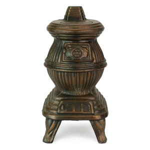 May include: A vintage cast iron stove shaped pencil sharpener with a dark brown finish. The sharpener has a decorative design on the front and a small opening for pencils.