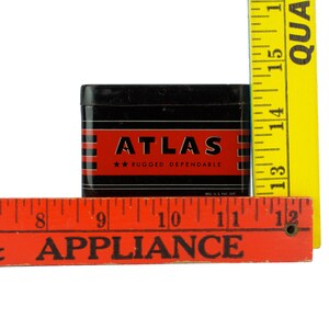 K&ouml;nnte beinhalten: Eine schwarze Metalldose mit einem rot-wei&szlig; gestreiften Design. Die Dose tr&auml;gt die Aufschrift "ATLAS" in wei&szlig;en Buchstaben und "RUGGED DEPENDABLE" in kleineren wei&szlig;en Buchstaben. Die Dose steht auf einem roten Holzlineal mit der Aufschrift "& APPLIANCE".