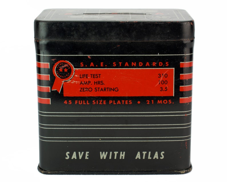 K&ouml;nnte beinhalten: Schwarze Metallbox mit roten und wei&szlig;en Streifen und dem Text "S.A.E. STANDARDS", "LIFE TEST", "AMP. HRS.", "ZERO STARTING", "45 FULL SIZE PLATES", "310", "100", "3.5", "21 MOS.", und "SAVE WITH ATLAS".