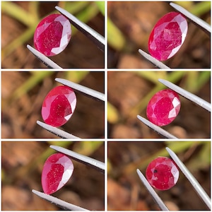 Może przedstawiać: Sześć zbliżeń fasetowanych rubinów o owalnym kształcie. Kamienie szlachetne są trzymane przez srebrne pęsety na rozmytym tle. Rubiny mają głęboki czerwony kolor i różne wewnętrzne wzory, pokazujące ich przejrzystość i szlif.