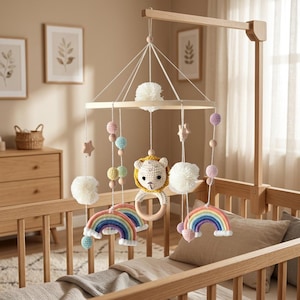 May include: A hanging crib mobile featuring a circular wooden frame with white pom-poms, crocheted rainbow arches in pastel colors, small wooden stars, and a central crocheted lion head attached to a smooth wooden ring, all suspended by white cords.