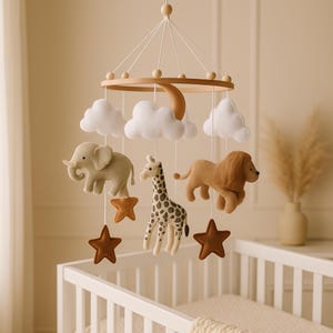 May include: A nursery mobile with a wooden frame, featuring felt animal figures including an elephant, giraffe, and lion, alongside white clouds and brown stars. The mobile hangs above a white cot.