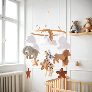 May include: A baby mobile featuring plush safari animals, including an elephant, giraffe, lion, and zebra, suspended from a wooden ring. White clouds and star shapes accompany the animals. The mobile hangs above a wooden crib in a bright room.