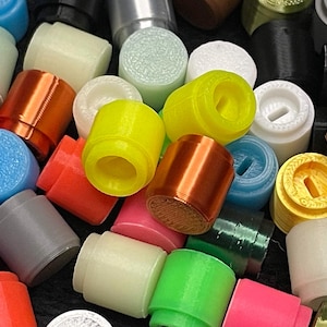 May include: A collection of colorful, cylindrical objects in various colors, including yellow, orange, blue, and green. The objects appear to be made of plastic or a similar material, with a smooth, rounded shape. Some have internal details.