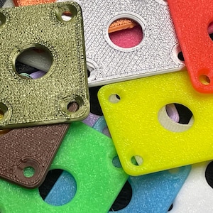 May include: Close-up of various colorful square plastic plates with a central circular hole and four smaller holes in the corners. Colors include green, yellow, red, silver, and brown. The plates have a textured surface.