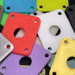 May include: A collection of colorful, textured, rectangular plastic pieces with a central hole and three smaller holes. Colors include red, white, gold, purple, blue, and green. The pieces are scattered, creating a vibrant display.