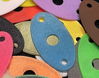 May include: A collection of colorful, oval-shaped 3D-printed objects with a hole in the center and a smaller hole at one end. The objects are in various colors, including blue, pink, orange, green, yellow, and purple. The objects have a textured surface.