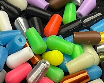 May include: A collection of colorful, cylindrical objects in various shades including green, red, black, and silver. The objects appear to be made of plastic or a similar material, with a smooth, rounded shape. The assortment is scattered, creating a visually diverse display.