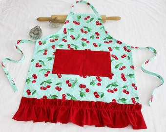 May include: A turquoise and red apron with a cherry print and a red pocket. The apron has a ruffled hem.