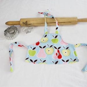 May include: A blue and white child's apron with a fruit print. The apron has two ties and is made of cotton fabric.