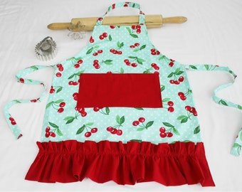 May include: A turquoise and red apron with a cherry print and a red pocket. The apron has a ruffled hem and ties at the neck and waist.