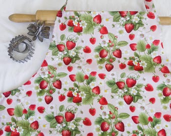May include: A pink apron with a strawberry print. The apron has adjustable straps and a large pocket in the front.