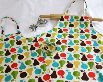May include: Two aprons with a colorful fruit pattern, featuring red, green, yellow, and blue apples and pears on a cream background. A wooden rolling pin and two metal cookie cutters are also present, suggesting a baking theme.