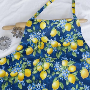 May include: A blue apron with a lemon and flower print. The apron has adjustable straps and a large pocket in the front.