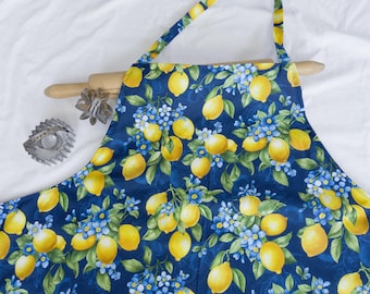 May include: A blue apron with a lemon and flower print. The apron has adjustable straps and a large pocket in the front.